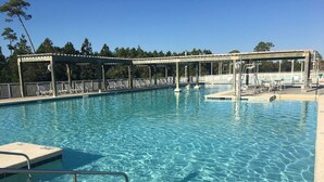 Una piscina cristalina con terraza de madera y sillones de descanso, rodeada de árboles.