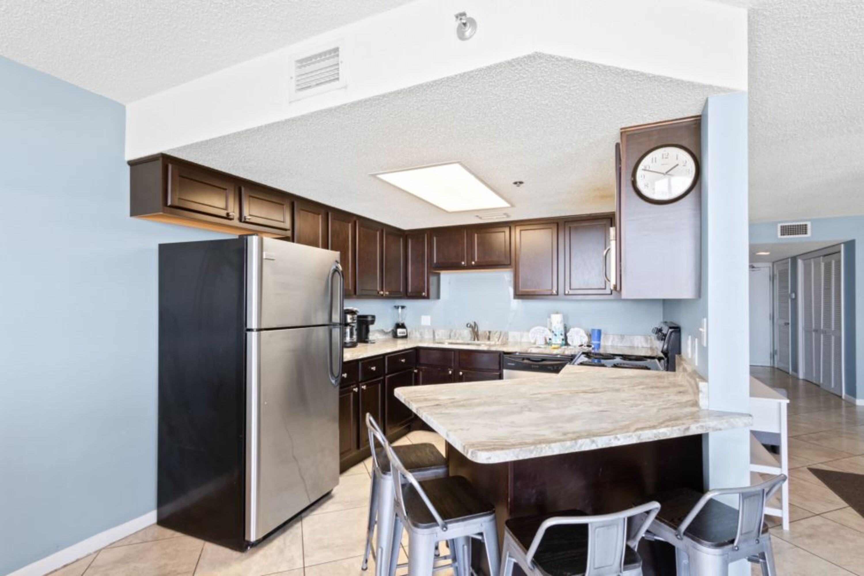 A modern kitchen with dark wooden cabinets, stainless steel appliances, and a marble countertop.