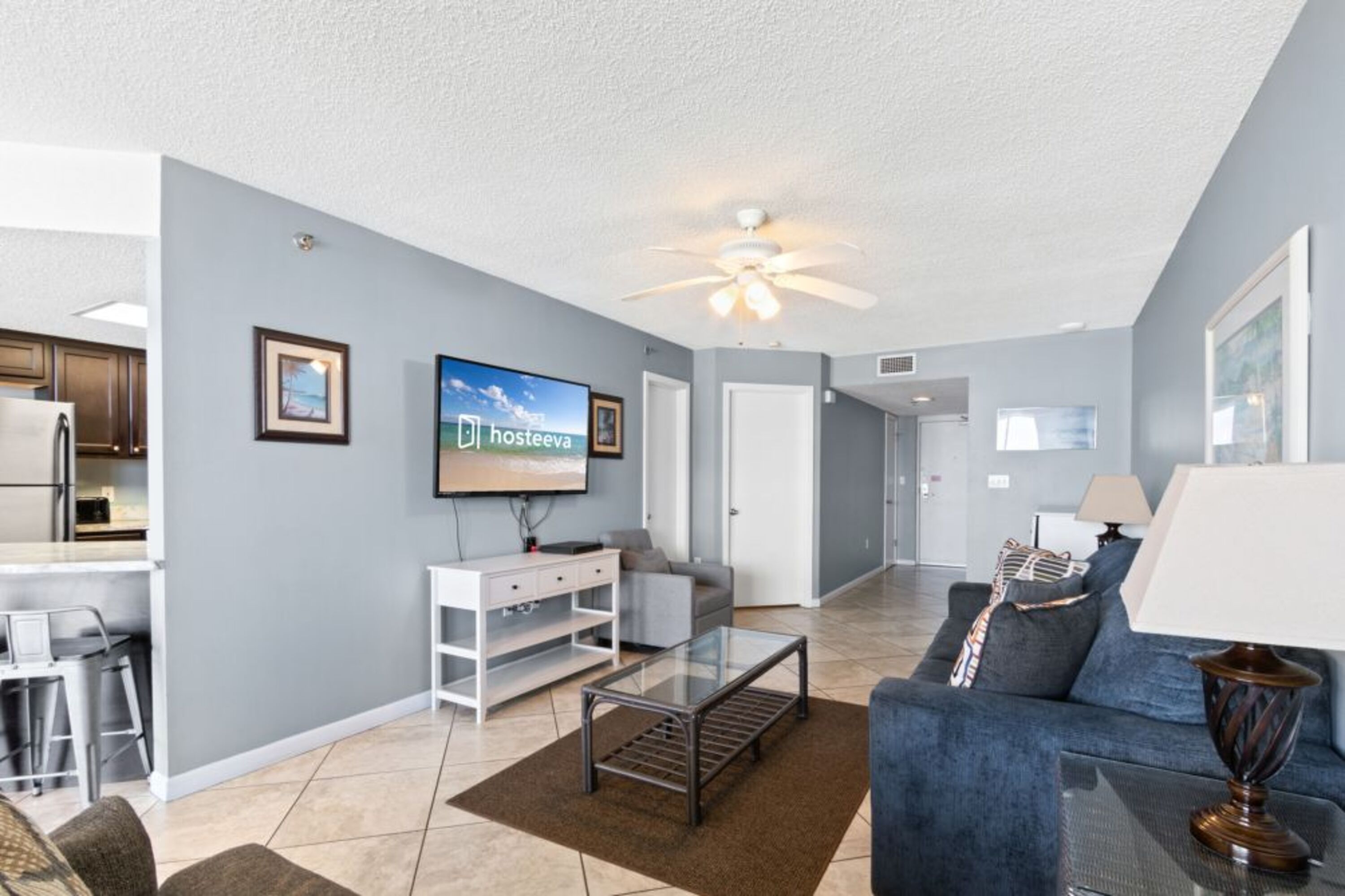 A modern living room with a flat-screen TV, a ceiling fan, and a sofa.