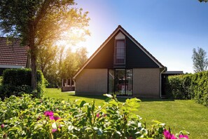 A modern house with a sloped roof, a glass door entrance, and a well-maintained garden with flowers and shrubs. - HVZ Orchis  6p - Three Bedroom Resort, Sleeps 6 (Heinkenszand)