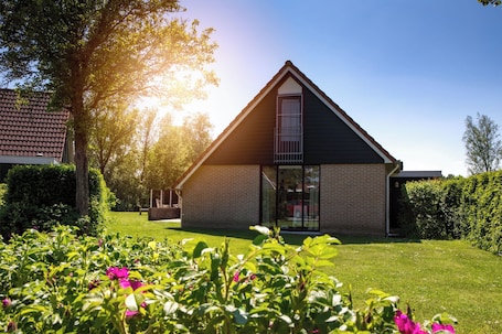 A modern house with a sloped roof, a glass door entrance, and a well-maintained garden with flowers and shrubs.