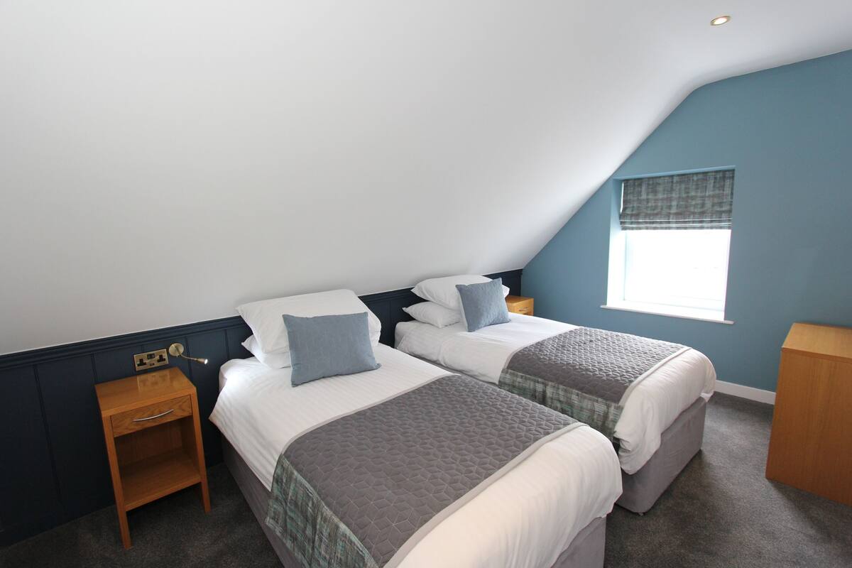 Ein Schlafzimmer mit zwei Betten, einem Nachttisch, einem Fenster mit Jalousien und einem Holznachttisch.