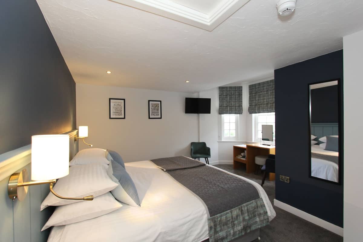 Ein Hotelzimmer mit Bett, Schreibtisch, Stuhl, Flachbildfernseher und einem Fenster mit Jalousien.