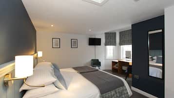 A hotel room with a bed, a desk, a chair, a flat-screen TV, and a window with blinds.