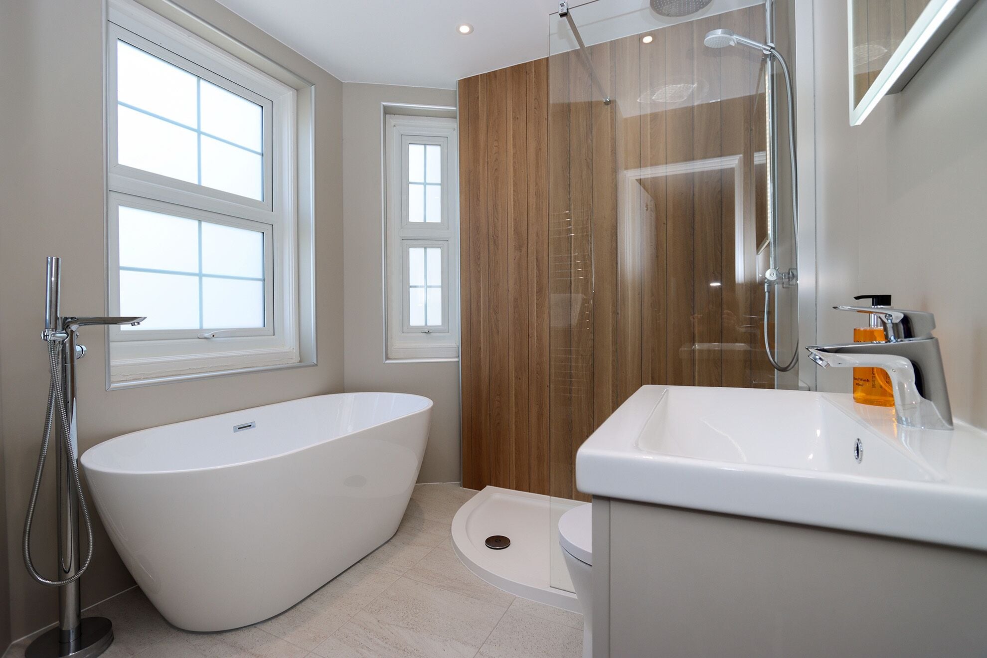 A modern bathroom with a freestanding bathtub, a shower enclosure, and a sink with a soap dispenser.
