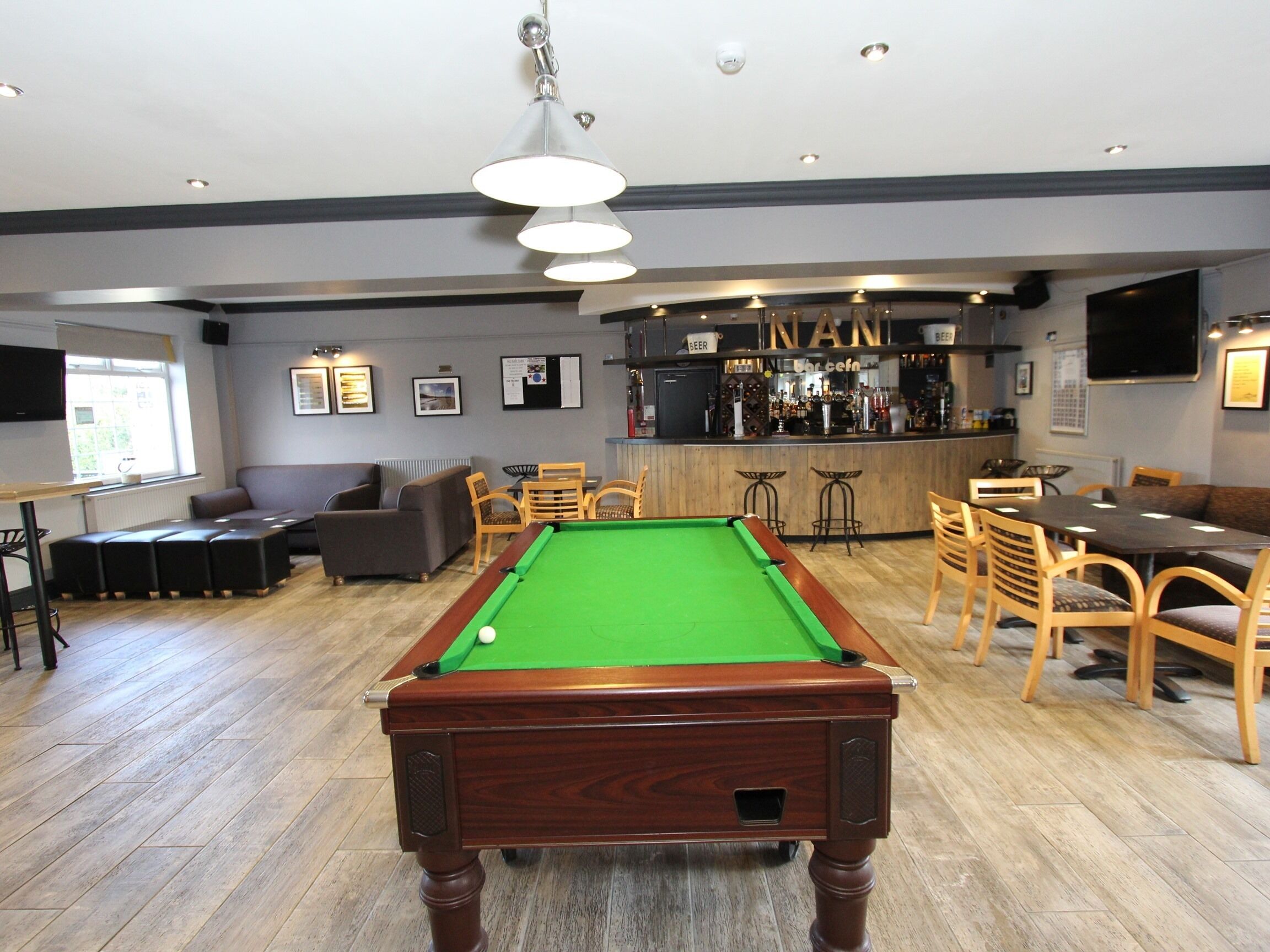 A pool table in a room with a bar area, seating, and a television mounted on the wall.
