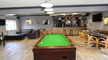 A pool table in a room with a bar area, seating, and a television mounted on the wall.
