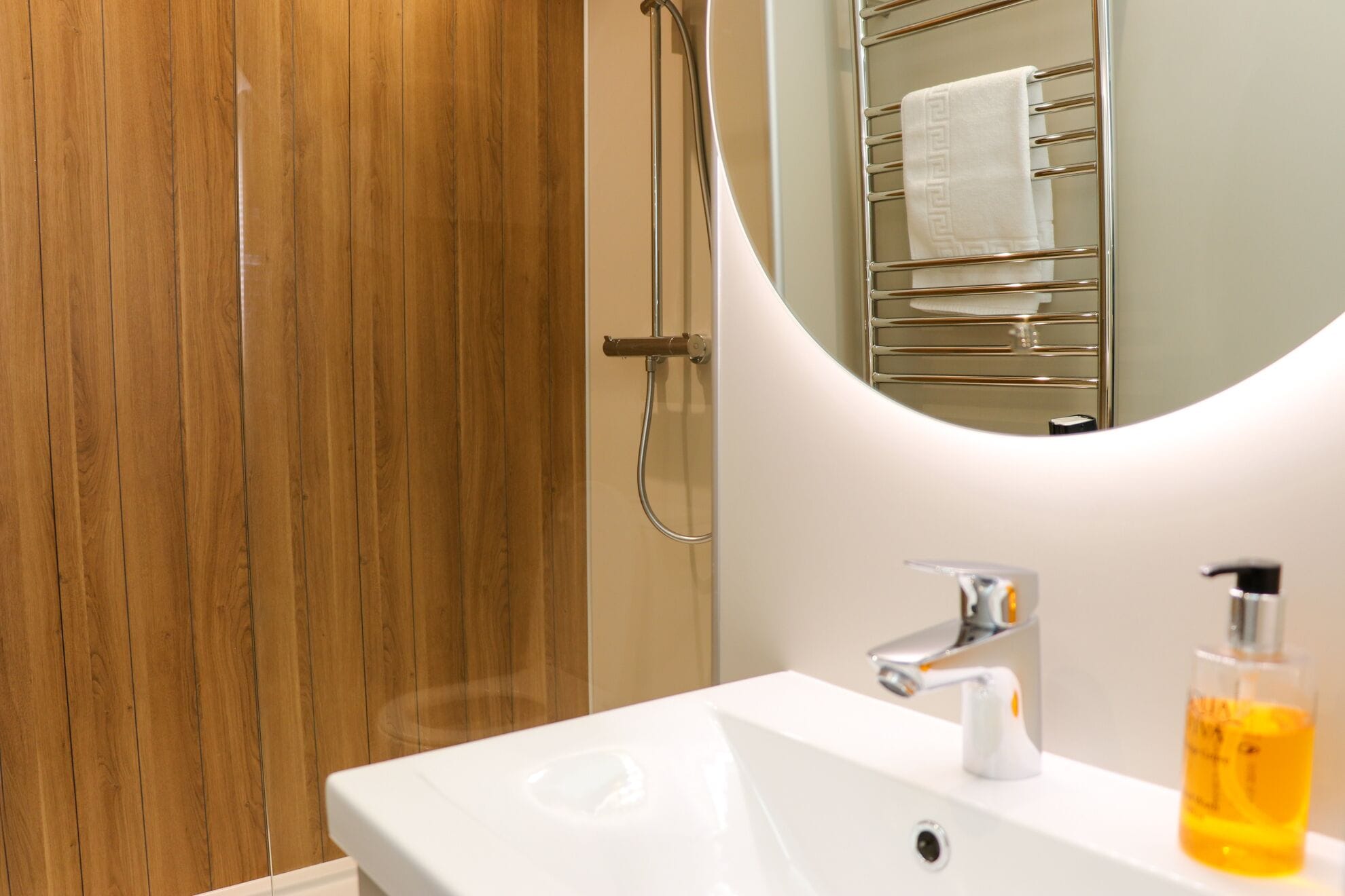 Un baño con puerta de madera, ducha, lavamanos con grifo y espejo con toallero.