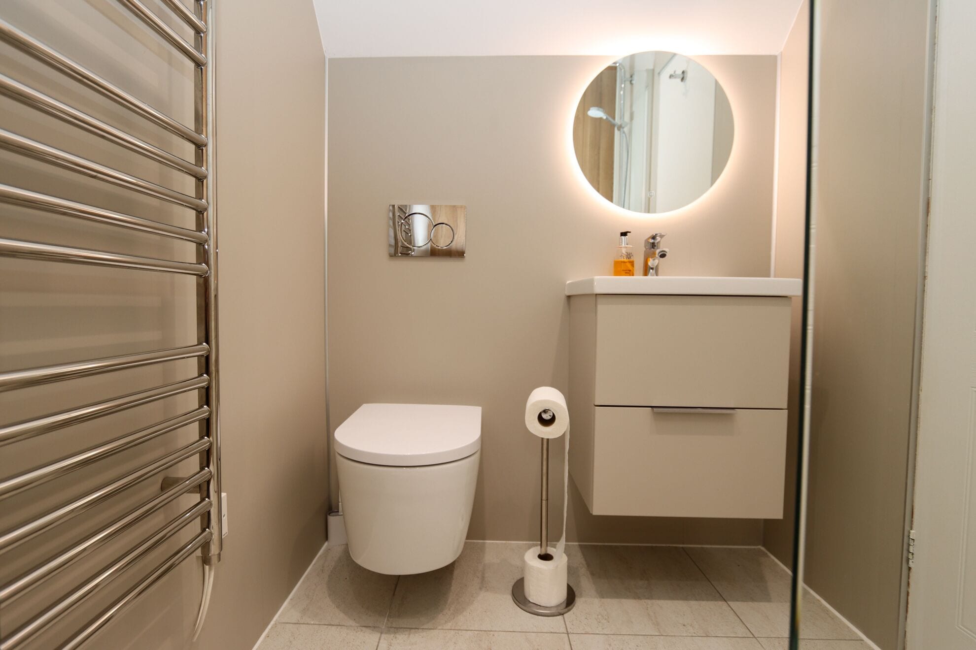 Un baño con inodoro, bidé, lavabo con espejo y dispensador de papel higiénico.