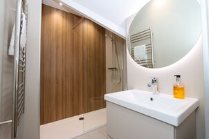 A modern bathroom with a wooden shower enclosure, a white sink with a mirror, and a bottle of hand soap.