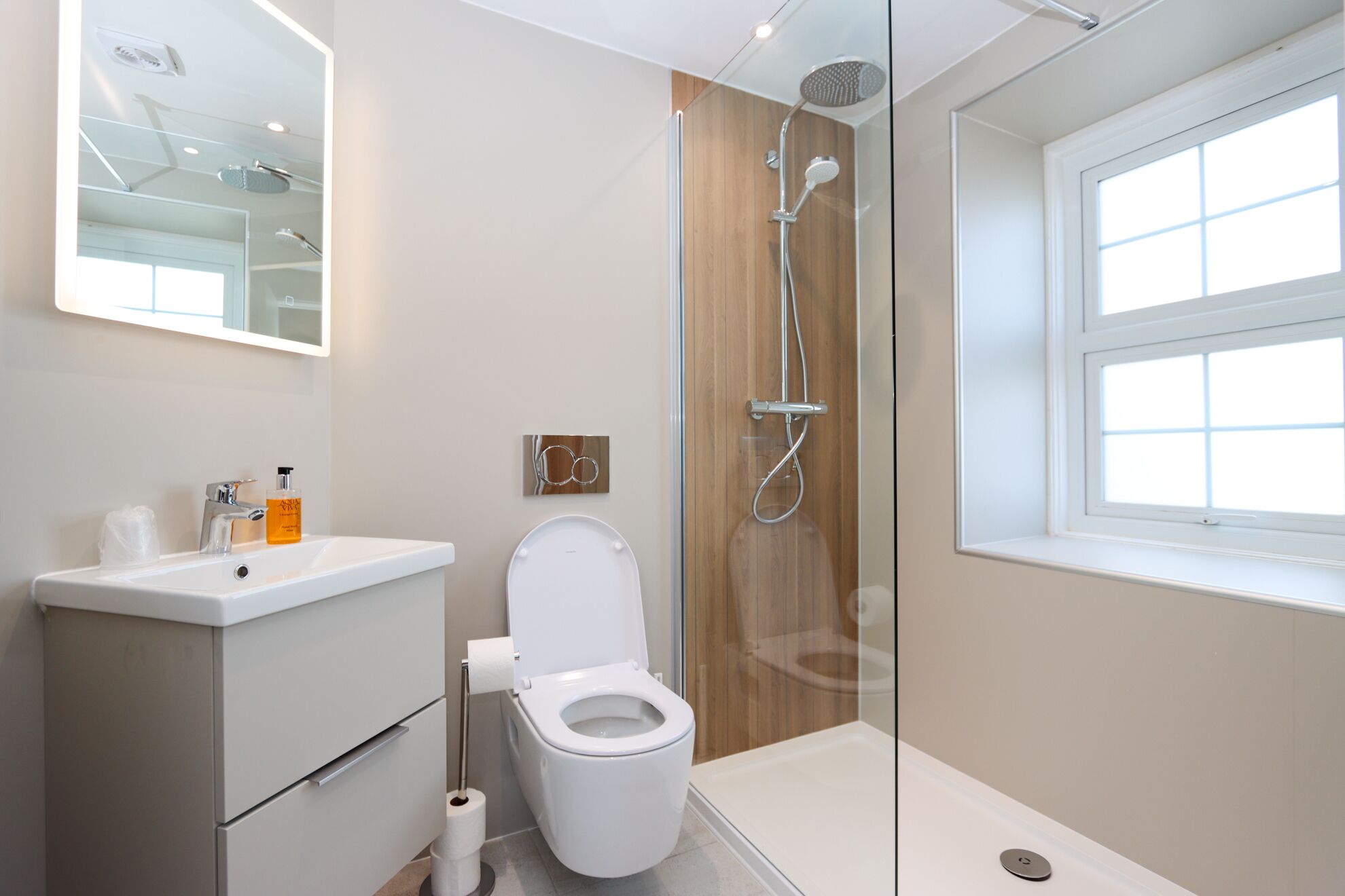 A modern bathroom with a toilet, sink, shower, and a window.