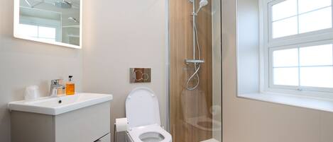 A modern bathroom with a toilet, sink, shower, and a window.