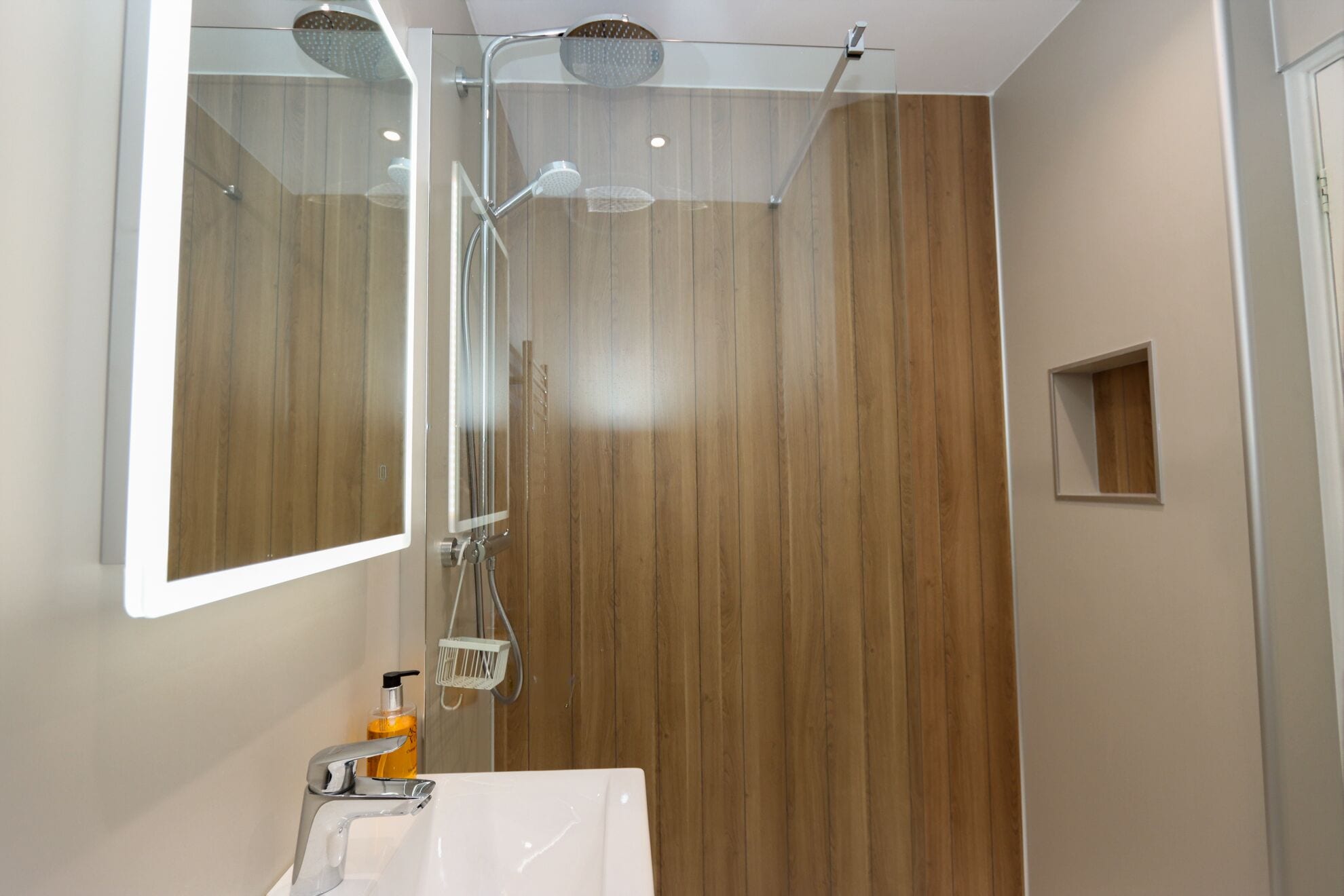 Une salle de bain moderne avec un mur recouvert de panneaux en bois, une douche en verre et un lavabo blanc doté d’un robinet chromé.
