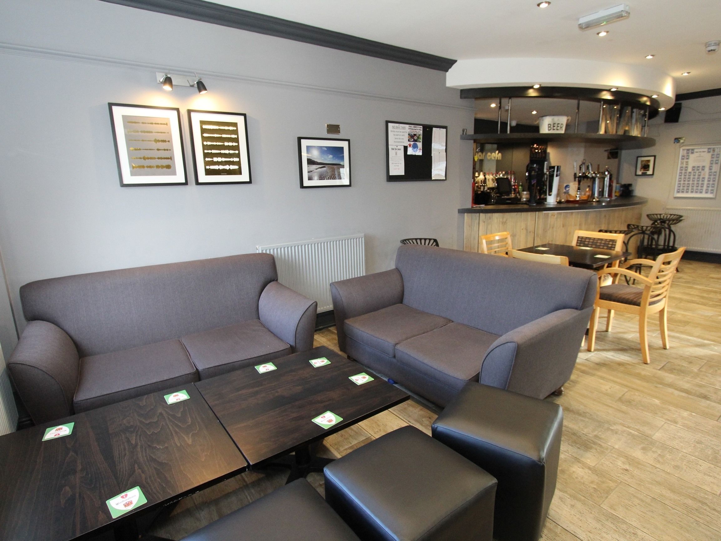 Un moderno salón con sofás grises, una mesa de centro de madera y una zona de bar con diversas botellas.