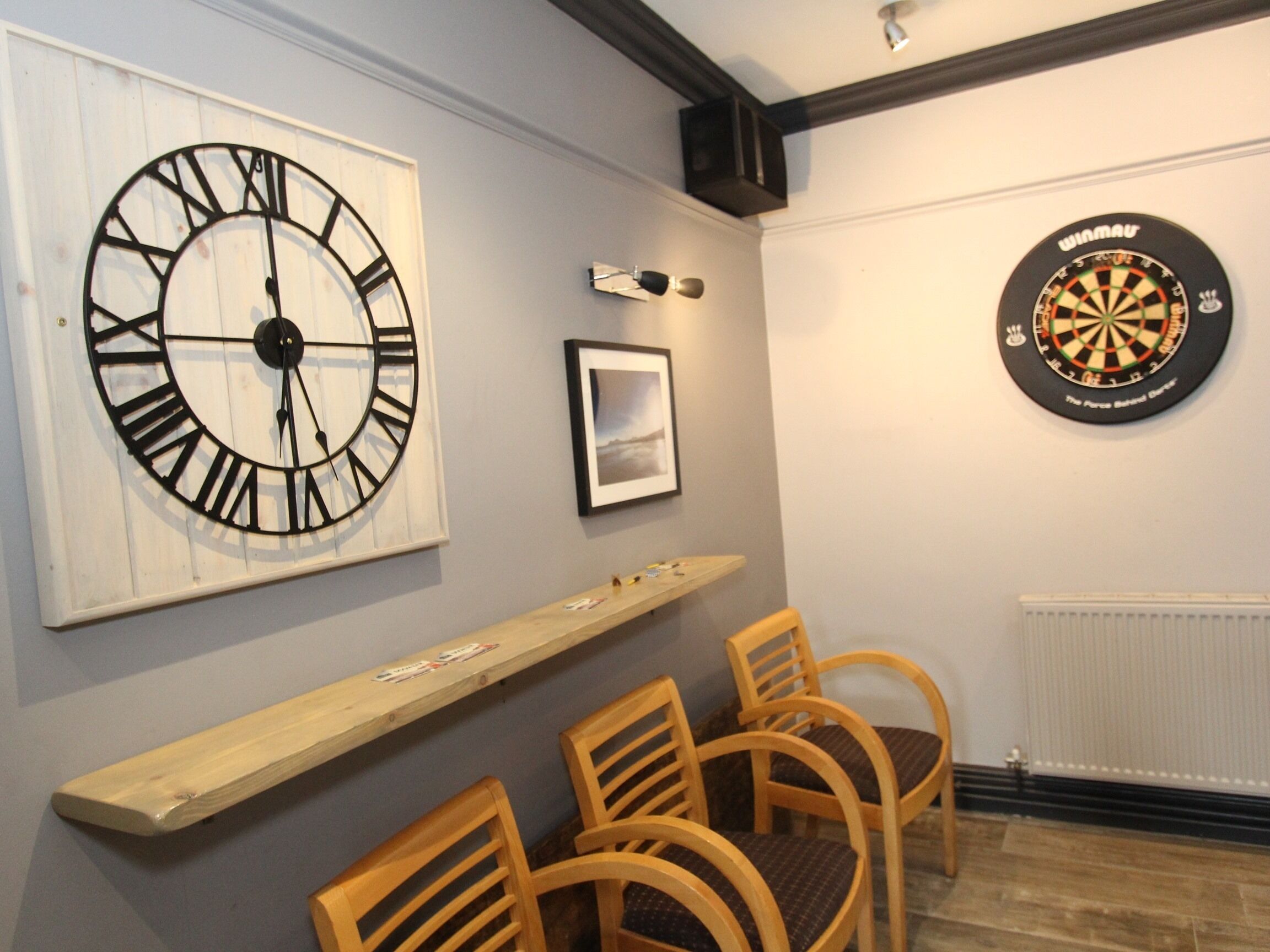 A room with a large wall clock, a dartboard, and a framed picture.