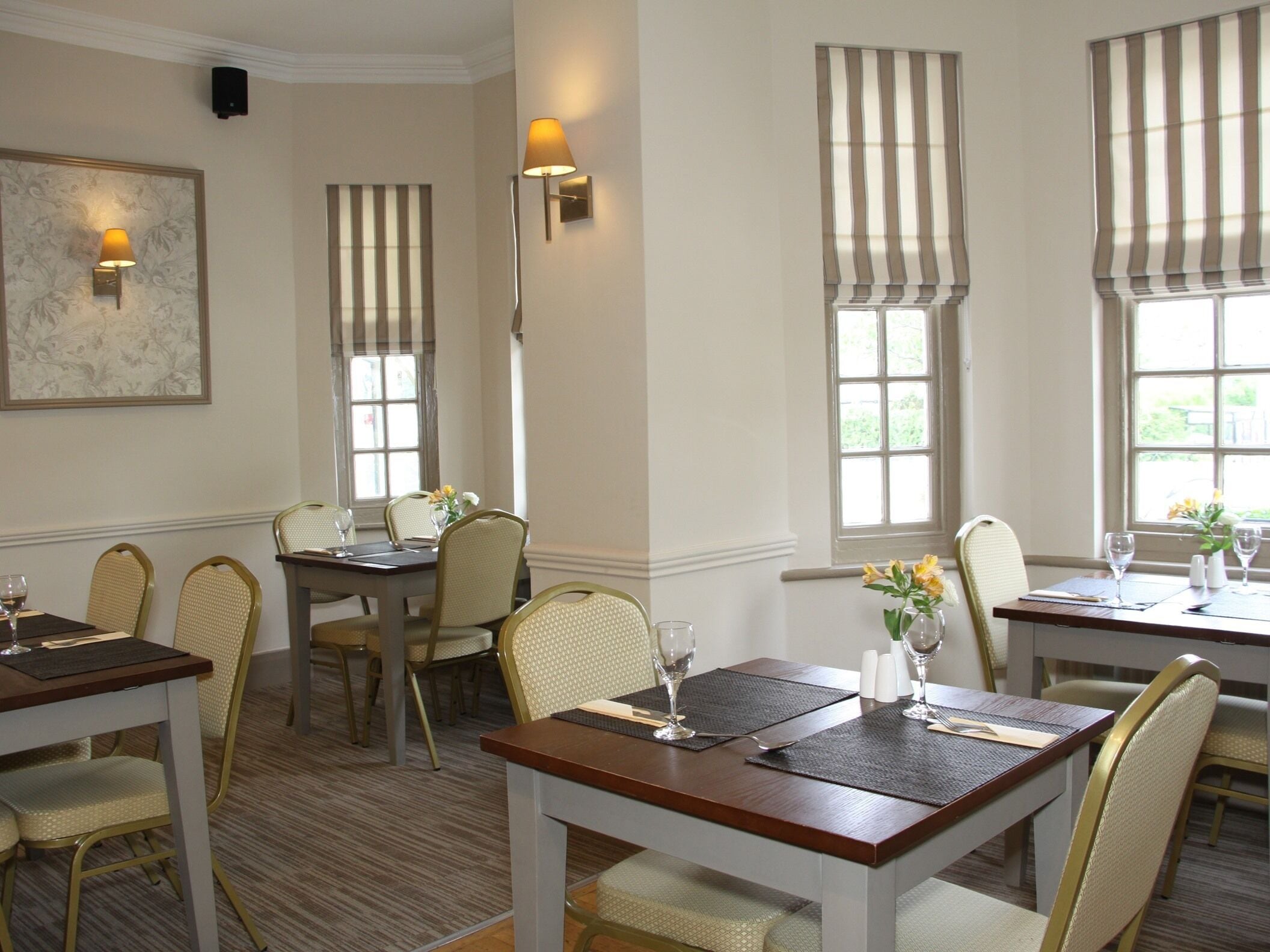 A dining area with tables and chairs, a wall-mounted light fixture, and a window with striped curtains.