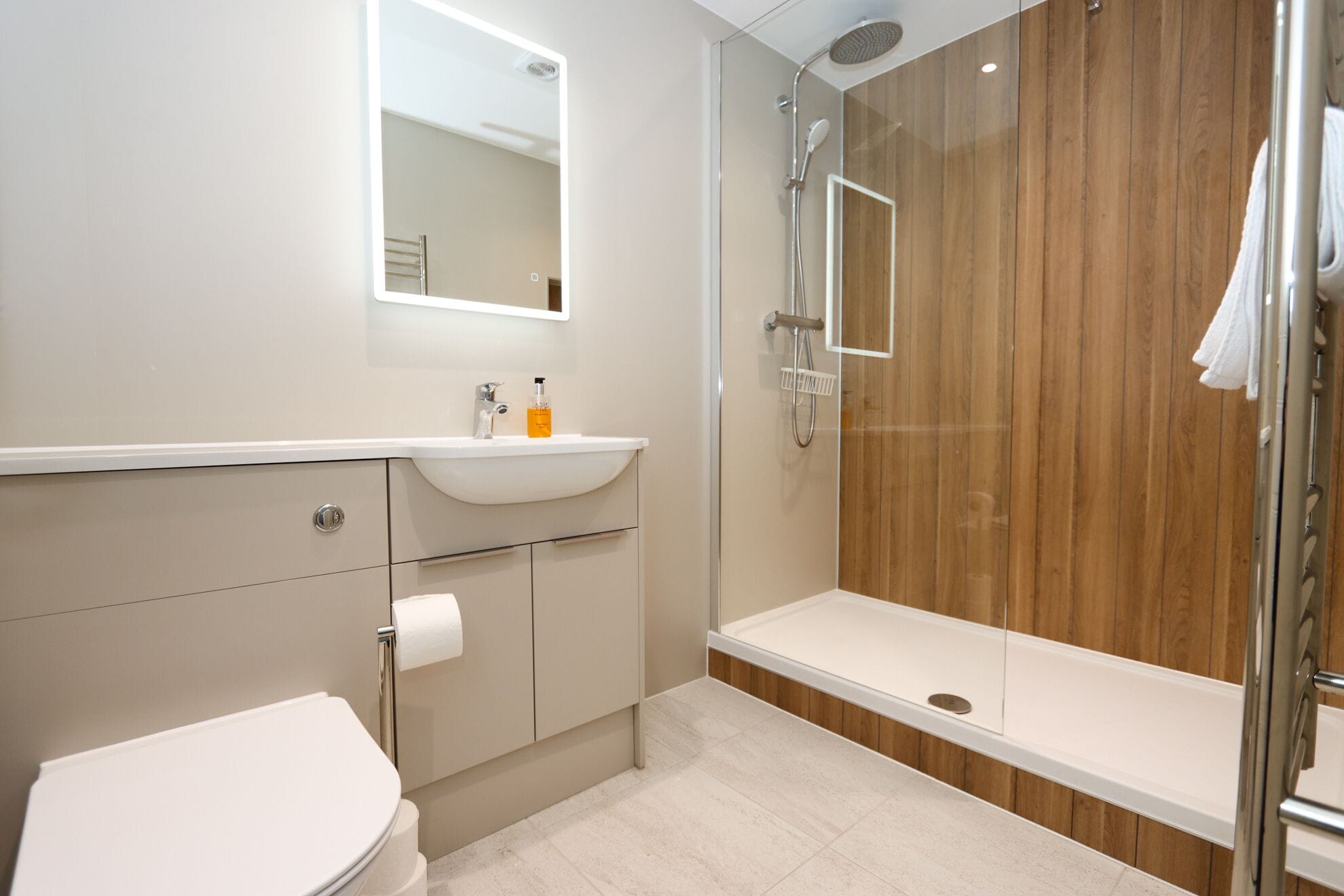 A modern bathroom with a toilet, sink, mirror, shower, and a wooden wall.