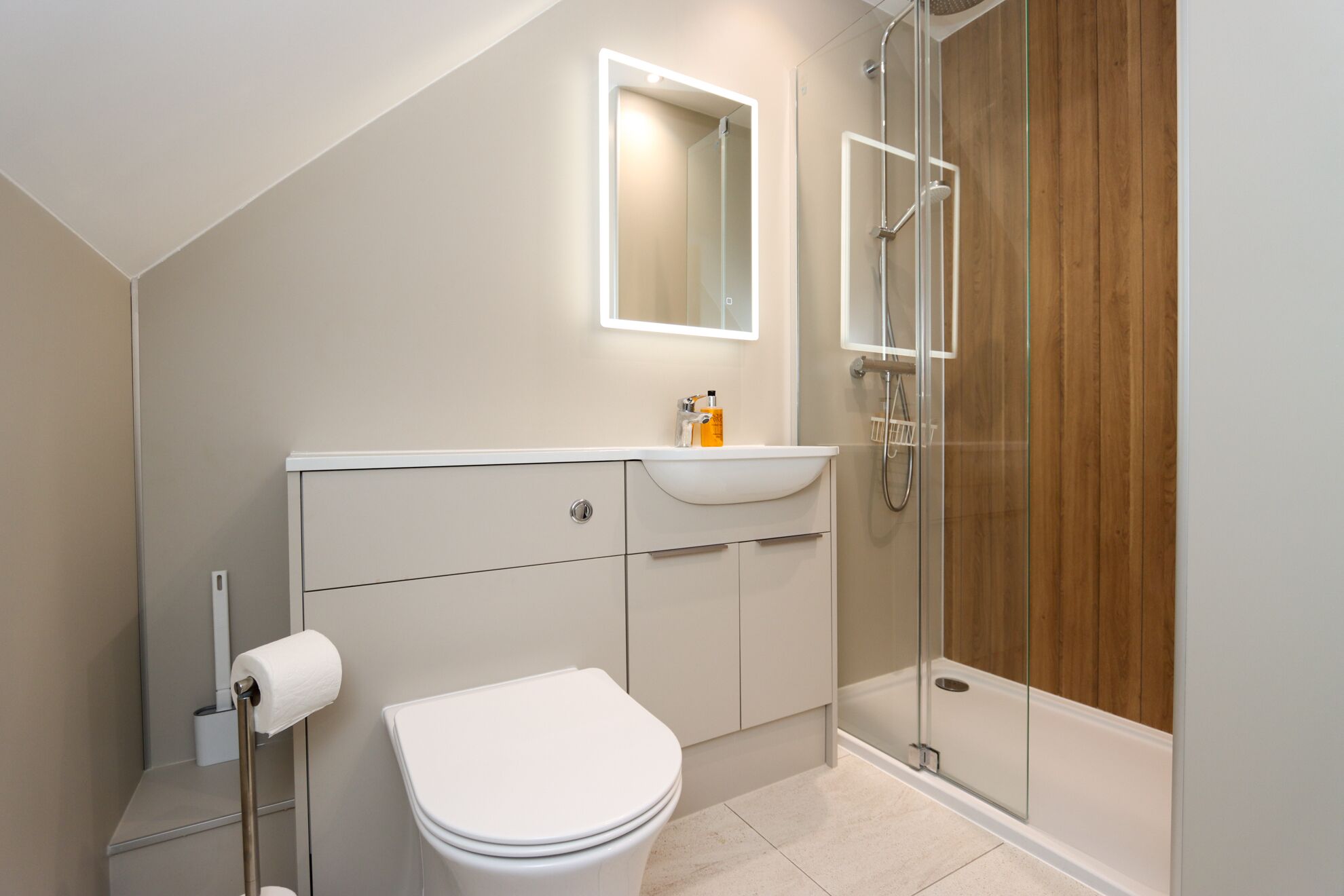 A modern bathroom with a toilet, sink, mirror, and shower.