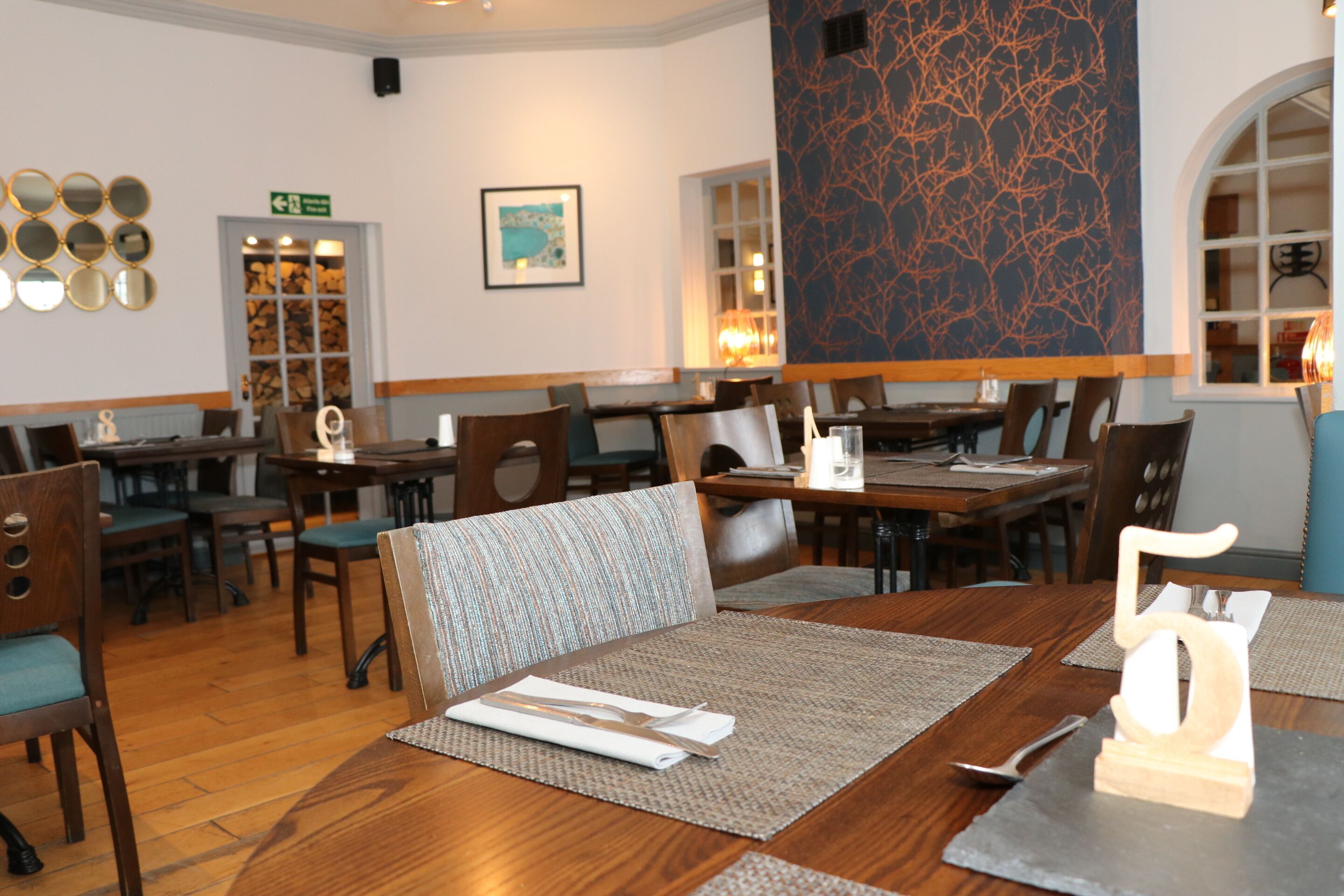 Ein Restaurant mit Holztischen und -stühlen, einem großen Wandbild und einem gerahmten Bild an der Wand.