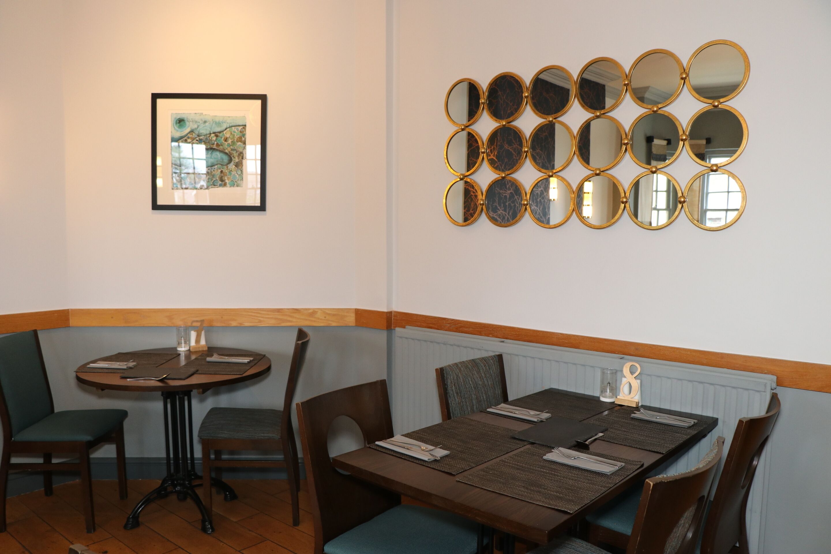 Un coin repas avec une table et des chaises en bois, un tableau encadré au mur et une rangée de miroirs ronds.