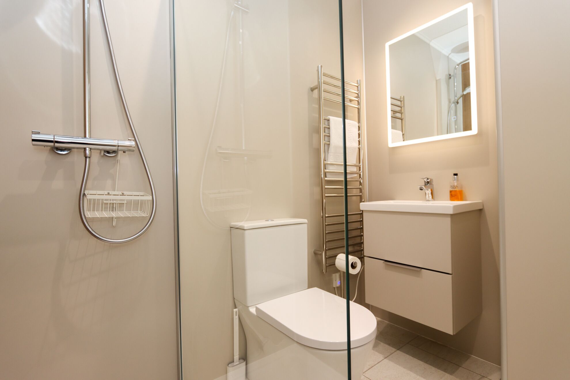 Un baño moderno con cabina de ducha de vidrio, inodoro blanco, tocador con espejo y toallero.