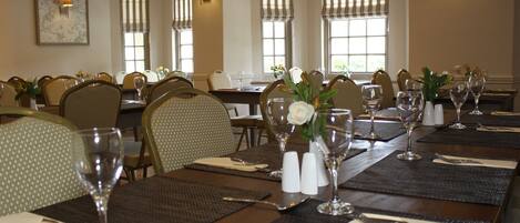 Une salle à manger avec plusieurs tables dressées pour le service, chacune agrémentée d’un vase de fleurs, de salières et de poivrières, ainsi que de verres transparents.