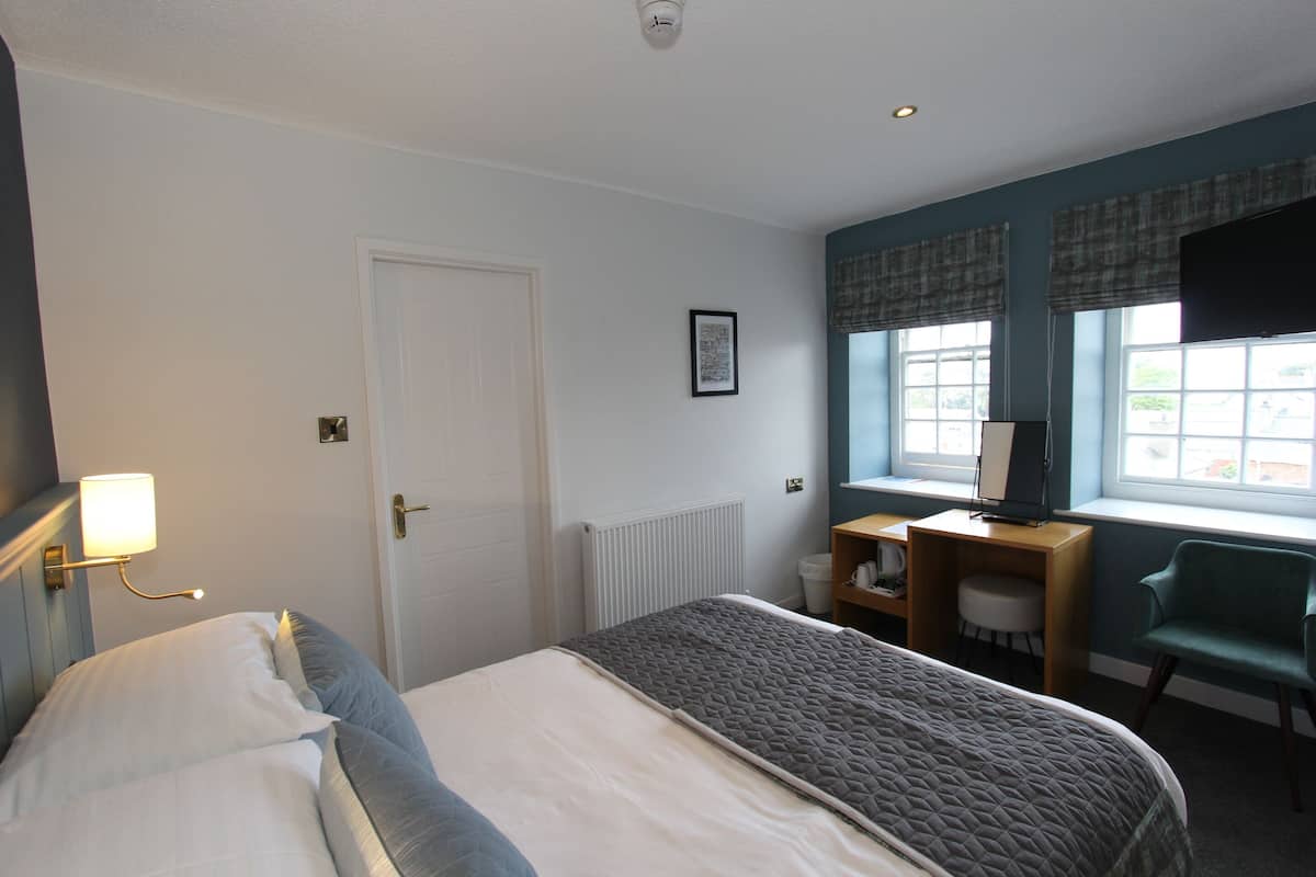 Ein Hotelzimmer mit einem Bett, einem Schreibtisch mit Computer, einem Stuhl und einem fenster mit Vorhängen.