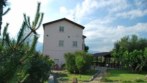 A two-story building with a flat roof, surrounded by a stone wall, a small garden, and a wooden structure. - Dante/Pino - Two Bedroom Apartment, Sleeps 6 (Tocco da Casauria)