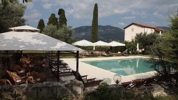 A pool area with lounge chairs and umbrellas, surrounded by trees and a mountain backdrop. - Dante/Pino - Two Bedroom Apartment, Sleeps 6 (Tocco da Casauria)
