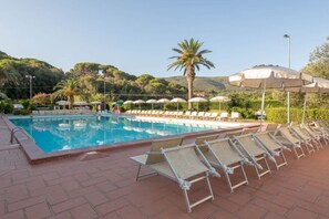 Ein Poolbereich mit Liegestühlen und Sonnenschirmen, umgeben von Grünflächen und Hügeln.