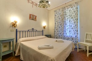 Ein Schlafzimmer mit einem Bett, einem Nachttisch, einem Sessel, einem kleinen Tisch, einem Gemälde und einer Chandelier.