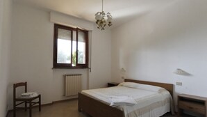 A bedroom with a single bed, a chair, a radiator, a window, and a wall-mounted light fixture.
