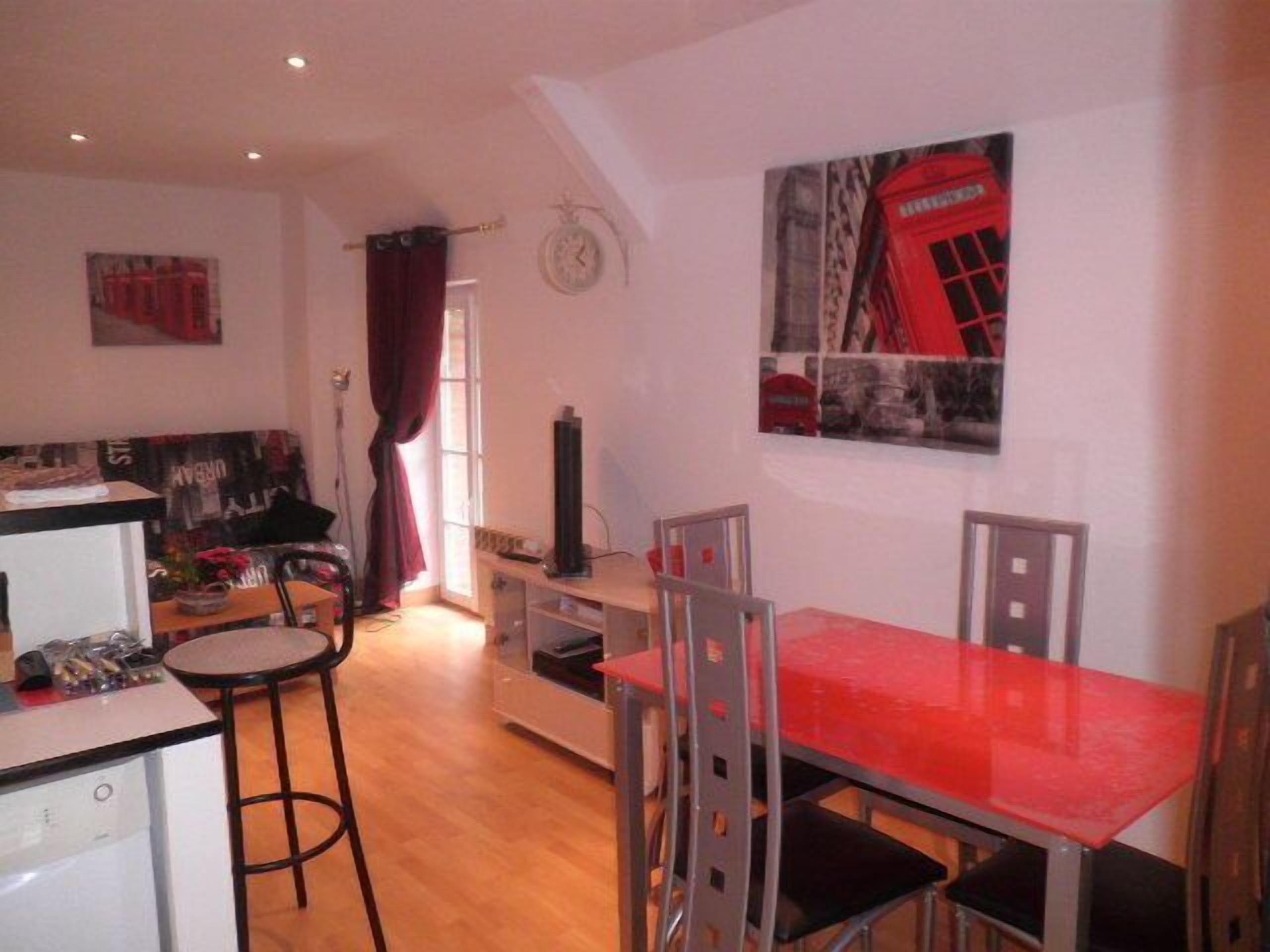 Un espace de vie compact comprenant un coin cuisine, un coin repas avec une table rouge et un salon avec un canapé et un rideau rouge.