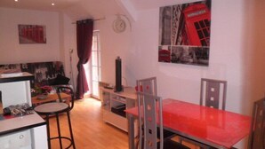 Een knus woongedeelte met een kitchenette, een eethoek met een rode tafel, en een woonkamer met een bank en een rood gordijn.