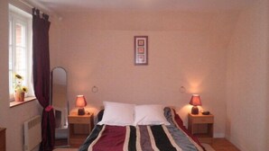 Een slaapkamer met een bed, twee bedlampen, een raam met gordijnen, een radiator en een ingelijst schilderij aan de muur.