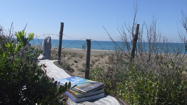 A beach with a barbed wire fence, a wooden structure, and a stack of books in the foreground. - Villa La Quercia-Dalia (Val Canina)