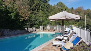 A swimming pool with lounge chairs and an umbrella, surrounded by trees and a stone wall. - Villa La Quercia-Dalia (Val Canina)