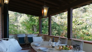A covered outdoor dining area with a table set for four, surrounded by chairs, and a view of trees and foliage. - Villa La Quercia-Dalia (Val Canina)
