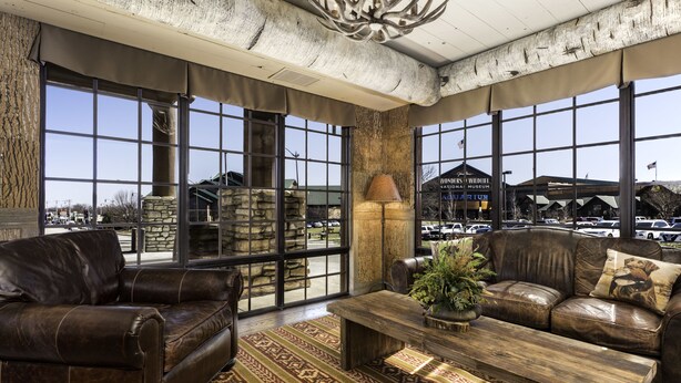 A spacious room with leather sofas, a wooden coffee table, and large windows offering views of the outside. - Bass Pro Shops Angler's Lodge (Springfield)