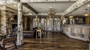 A rustic interior with exposed wooden beams, a stone fireplace, leather furniture, and a wooden bar area. - Bass Pro Shops Angler's Lodge (Springfield)
