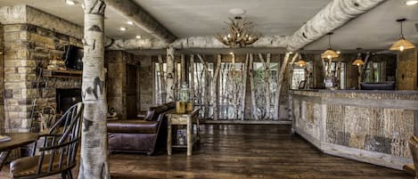 A rustic interior with exposed wooden beams, a stone fireplace, leather furniture, and a wooden bar area.