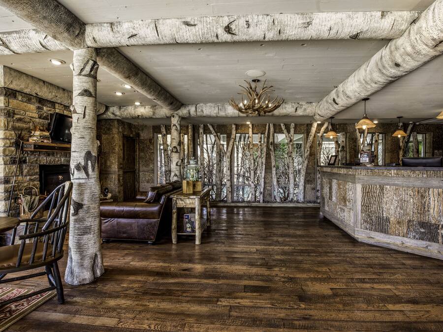 A rustic interior with exposed wooden beams, a stone fireplace, leather furniture, and a wooden bar area.