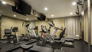 A gym with various exercise machines, a television mounted on the wall, and a clock.