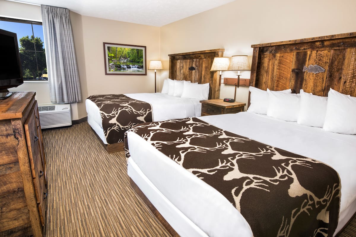 A hotel room with two beds, a TV, a desk, and a window with curtains.