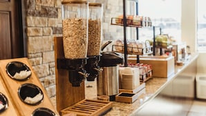 A coffee station with grinders and dispensers, a wooden counter, and a stone wall. - Bass Pro Shops Angler's Lodge (Springfield)