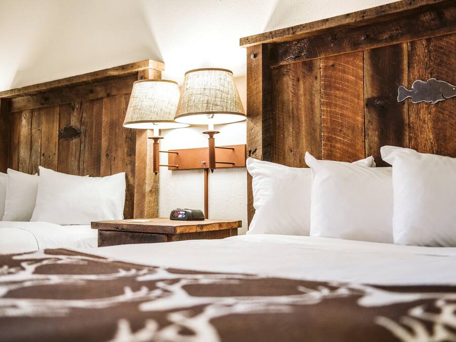 A neatly made bed with white linens, a wooden headboard, and two wall-mounted lamps.