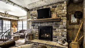A cozy living room with a stone fireplace, leather furniture, and a mounted television. - Bass Pro Shops Angler's Lodge (Springfield)