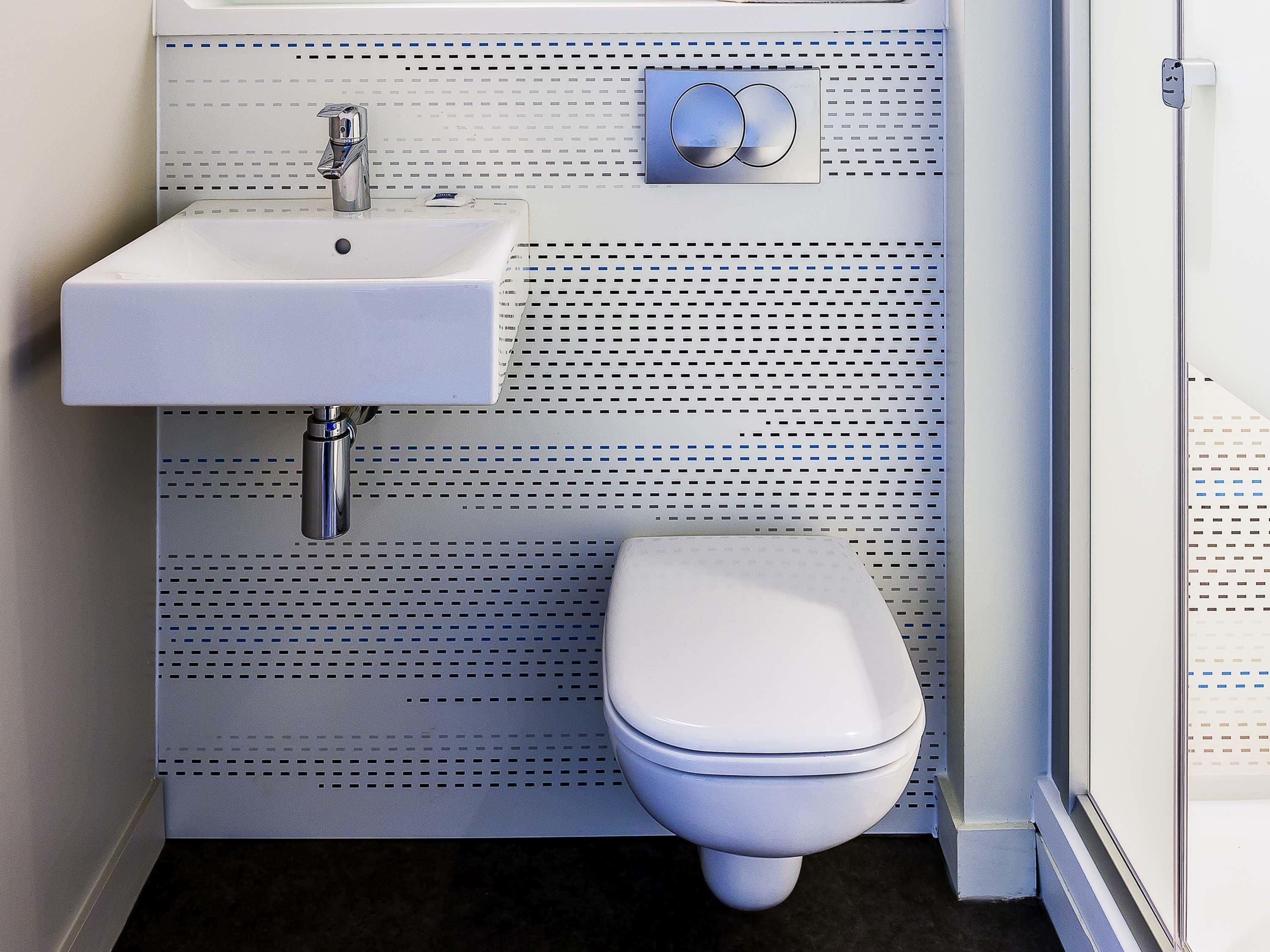 Une salle de bain avec un lavabo blanc, des toilettes et un bidet fixé au mur.