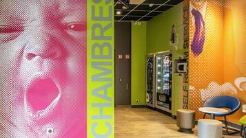 A brightly lit indoor space with a vending machine, seating area, and a wall with a large, colorful graphic.