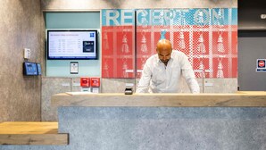 Un comptoir d’accueil doté d’un écran numérique, d’un plan de travail en bois et d’un mur orné d’un motif.